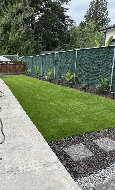 Artificial turf backyard installed by Top Gun Landscaping in Abbotsford, with planted borders along a privacy fence